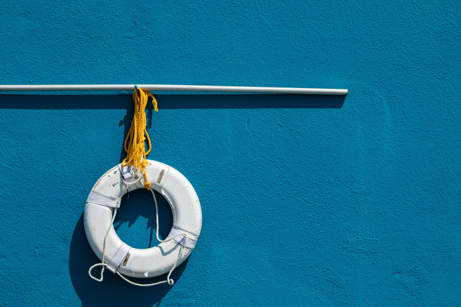 Das Bild zeigt einen weißen Rettungsring, der an einer Stange vor einer blauen Wand hängt | © Brian Breeden/Unsplash