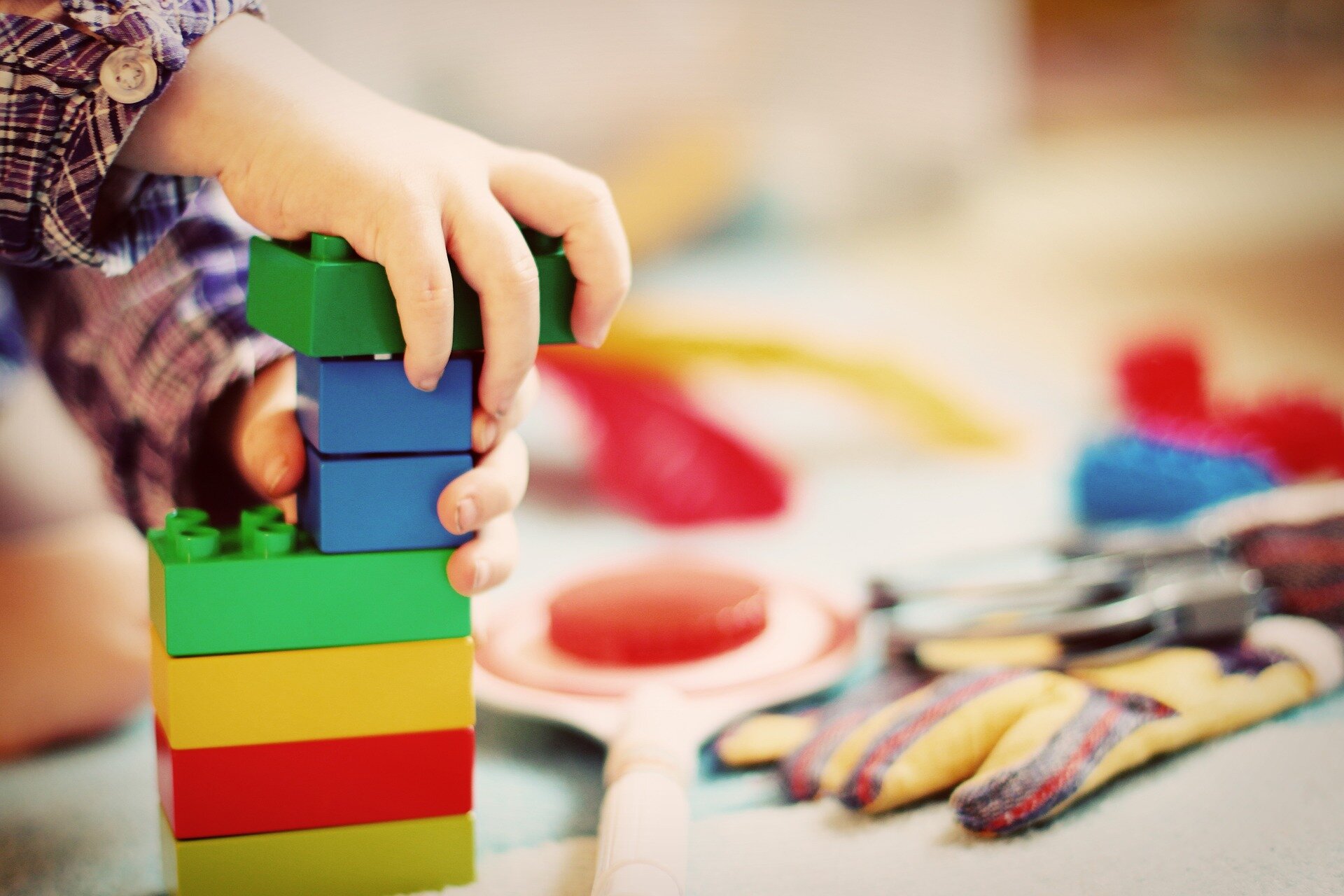 Auf dem Bild sieht man ein Kind, das gerade mit farbigen Plastikbauklötzen einen Turm baut. | © FeeLoona / Pixabay