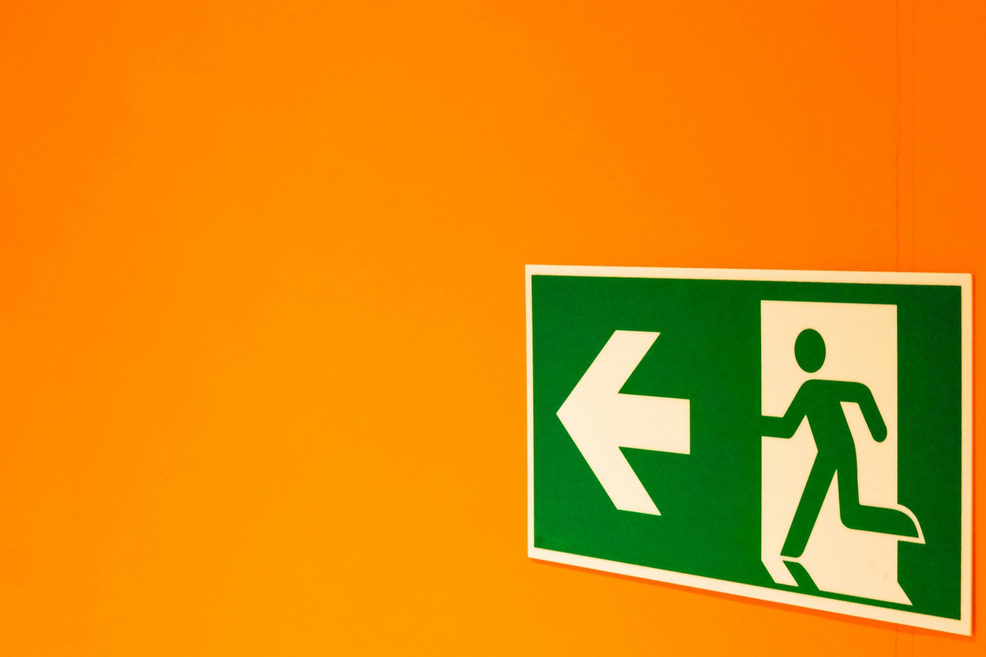 Das Bild zeigt ein Notausgang-Schild auf einer orangefarbenen Wand | © DDP/Unsplash
