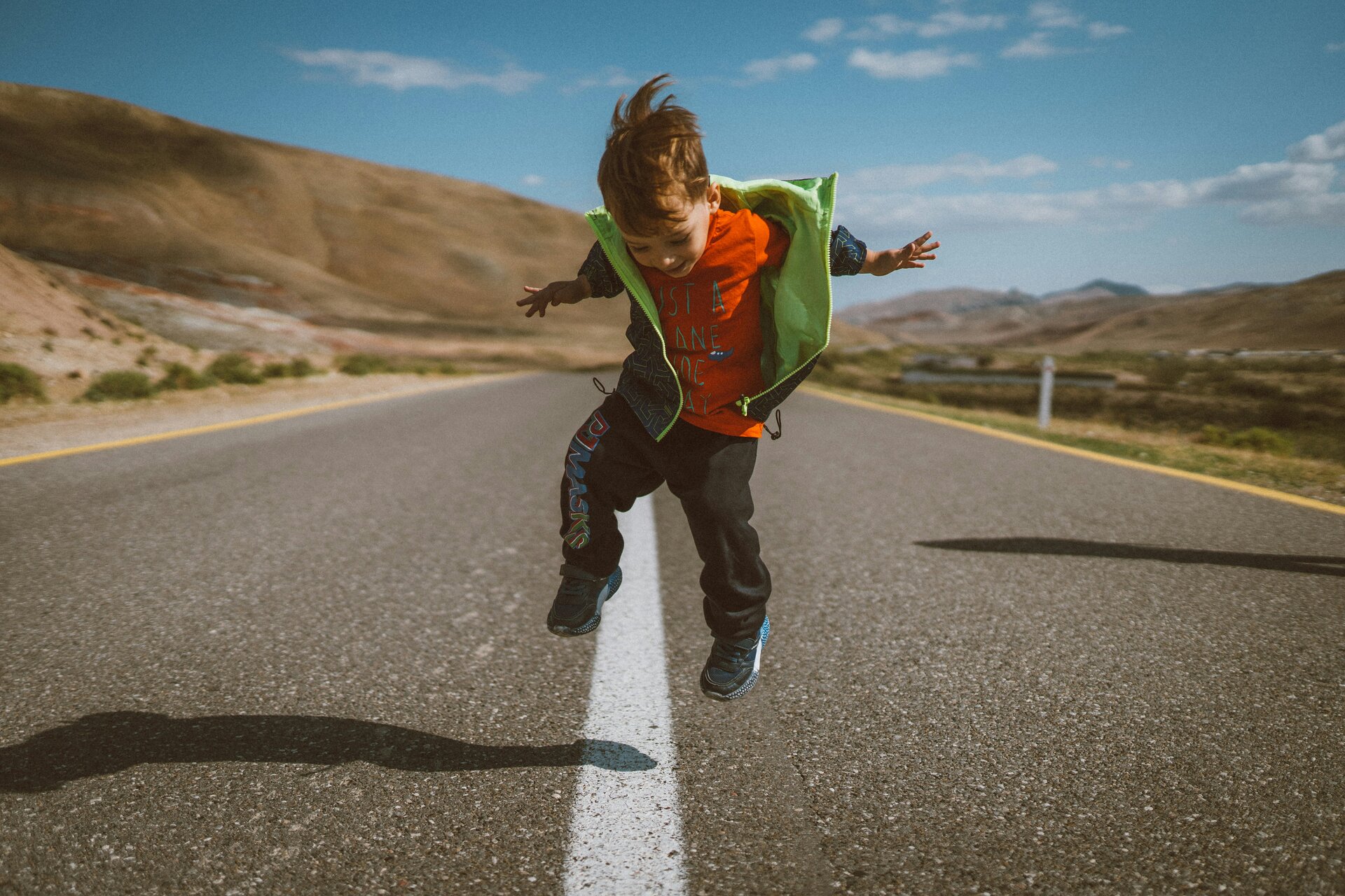 Das Bild zeigt einen Jungen, der auf einer Fahrbahn fröhlich auf dem Mittelstreifen springt | © Alvin Mahmudov/Unsplash