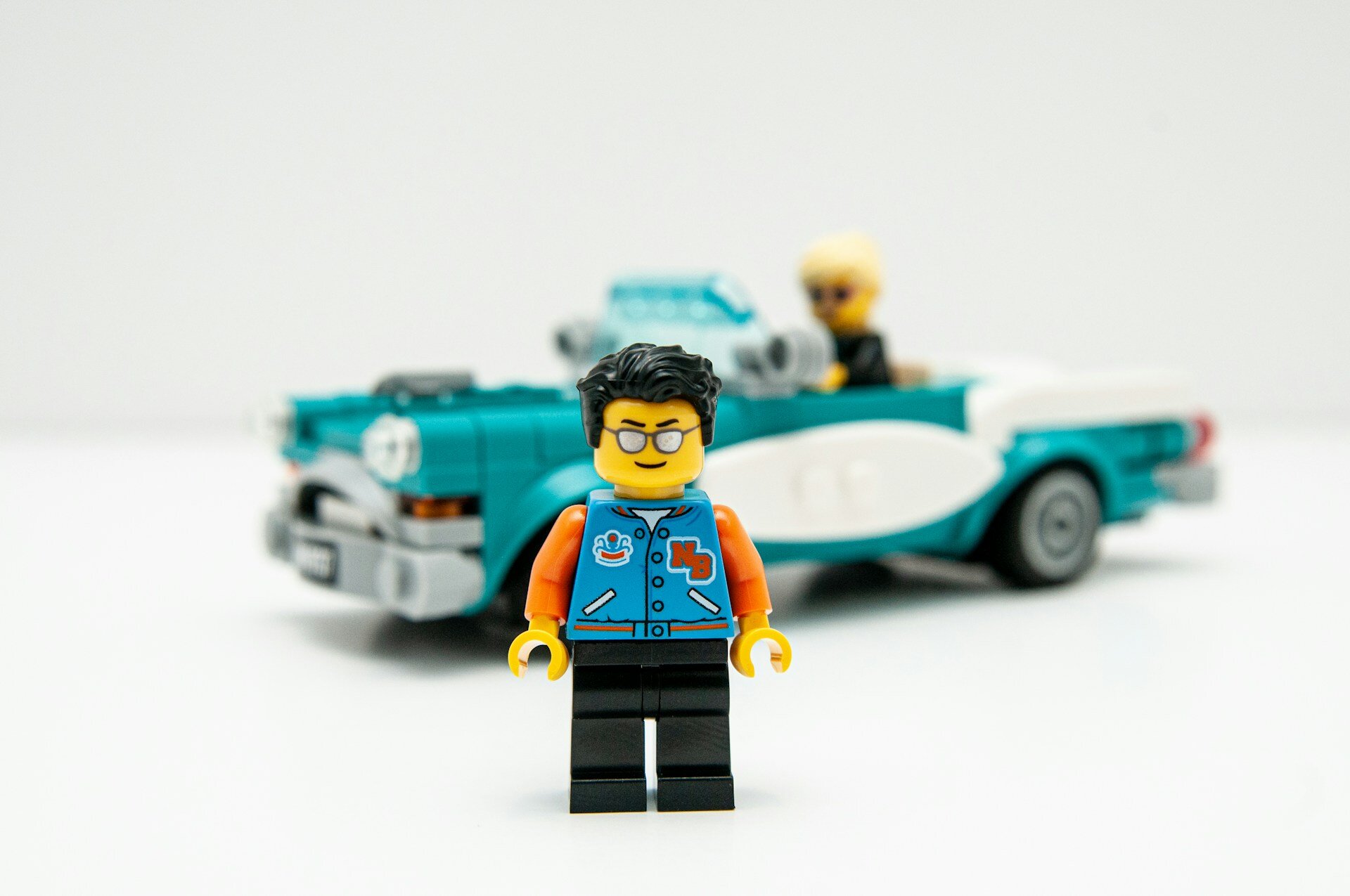 Auf dem Bild sieht man eine Legofigur mit einer Brille und blauen Jacke und im Hintergrund ein türkisfarbenes Legoauto mit einer Legofigur | © Matt Hudson/Unsplash