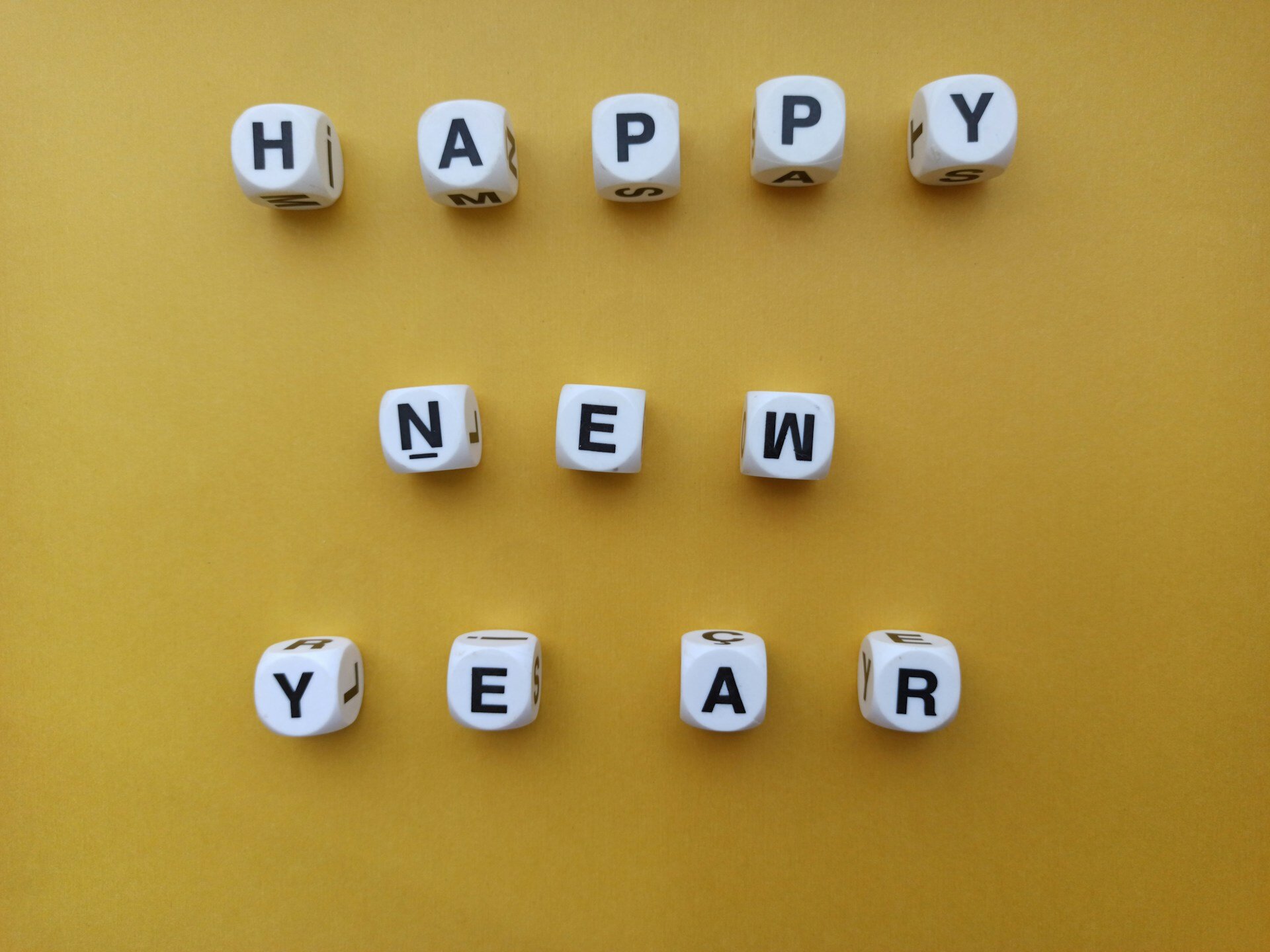 Auf dem Bild sieht man Würfel, die neben- und untereinander das Wort "Happy New Year" ergeben. Der Hintergrund ist gelb. | © Özgür Öztürk / Unsplash