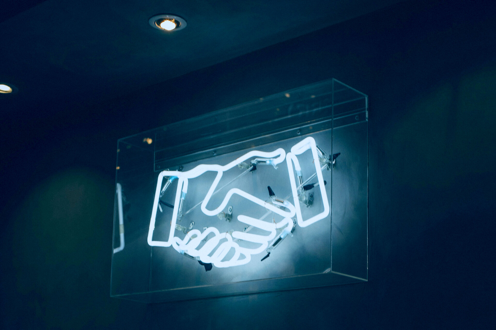 Auf dem Bild sieht man Neonröhren in der Form von einem Handschlag | © charlesdeluvio / Unsplash