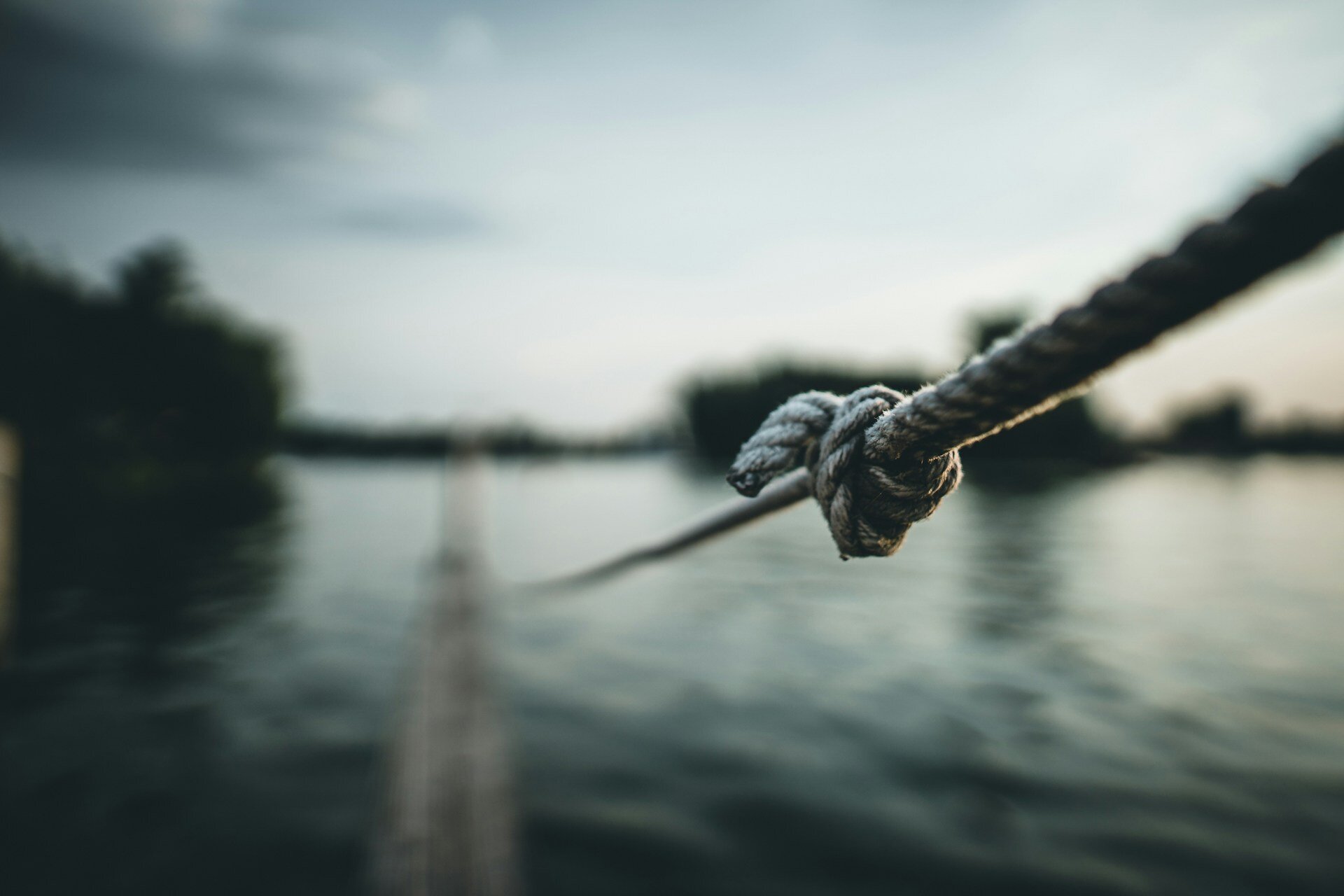 Auf dem Bild ist ein Seil mit einem Knoten zu sehen vor einem verschwommenen Hintergrund, der Wasser und einen Hafen erkennen lässt | © Max Saeling/Unsplash