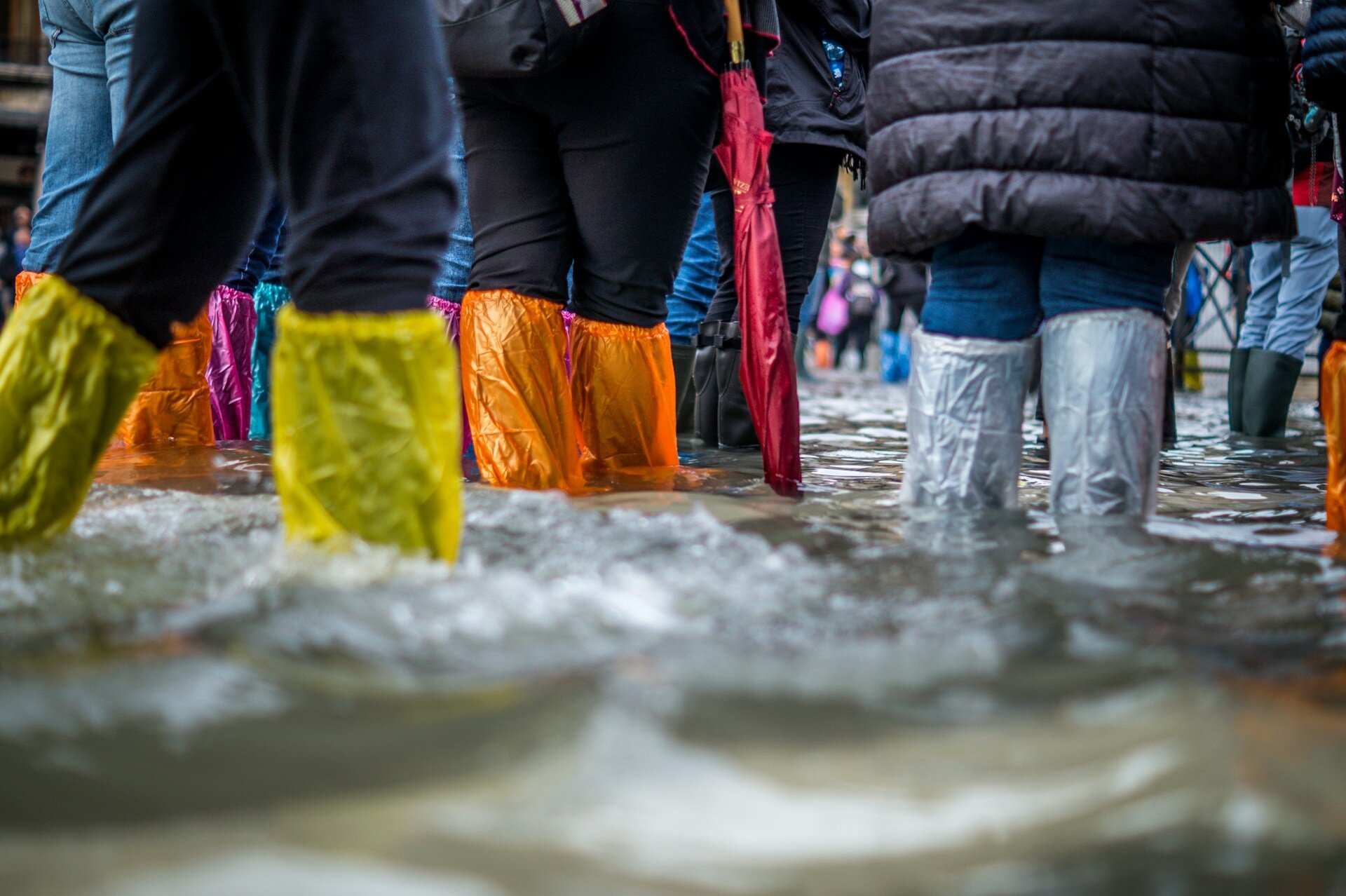 Auf dem Bild sieht man die Beiden von Menschen in bunten Gummiestiefeln durch eine überflutete Straße gehen. | ©  Jonathan Ford/Unsplash