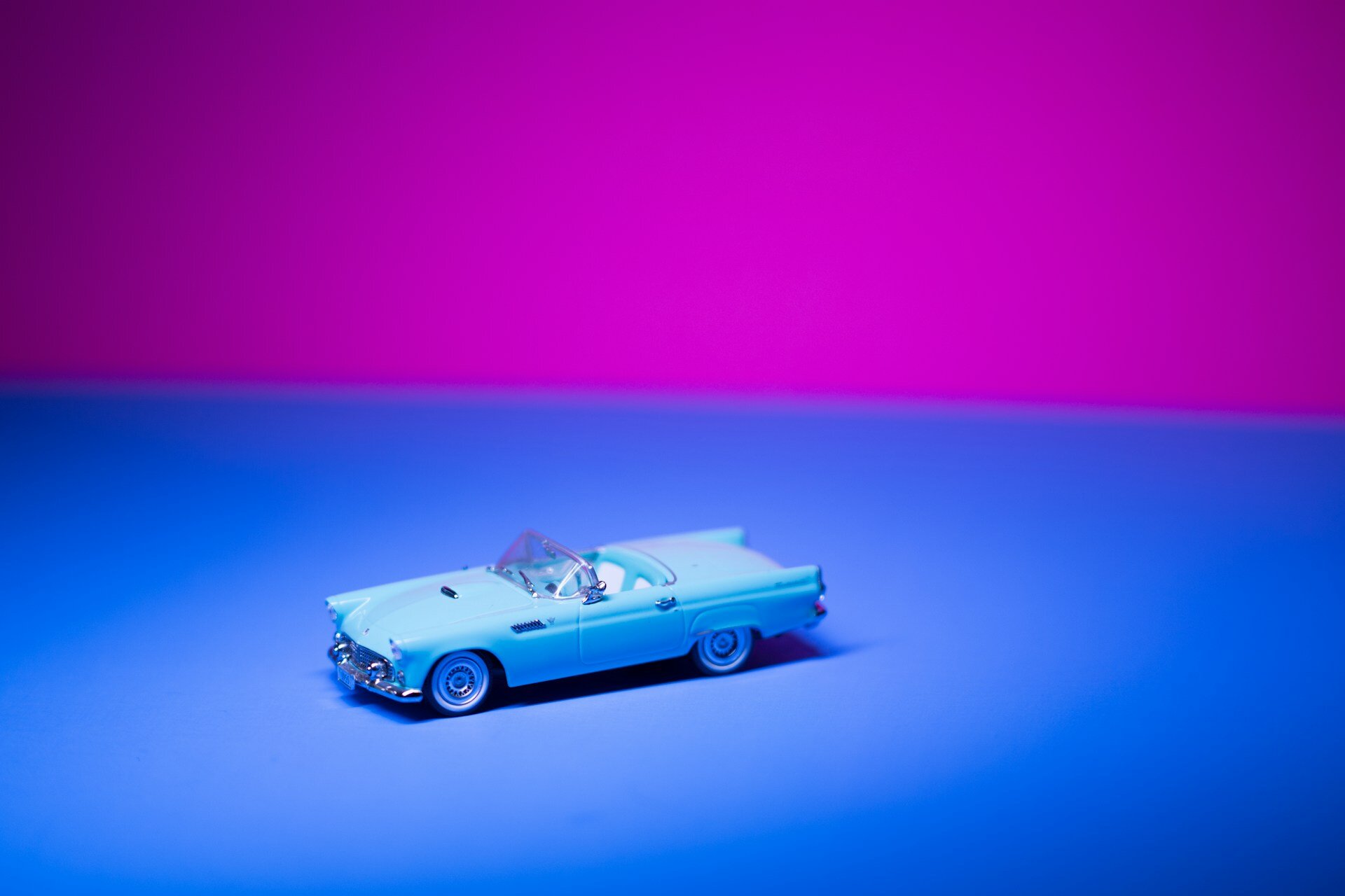 Auf dem Bild sieht man ein Cabrio-Spielzeugauto im Vintage-Optik. es ist klein, hellblau und steht vor einem blauen Boden, der obere Teil des Bildes ist lila. | © Ruvim Noga/Unsplash