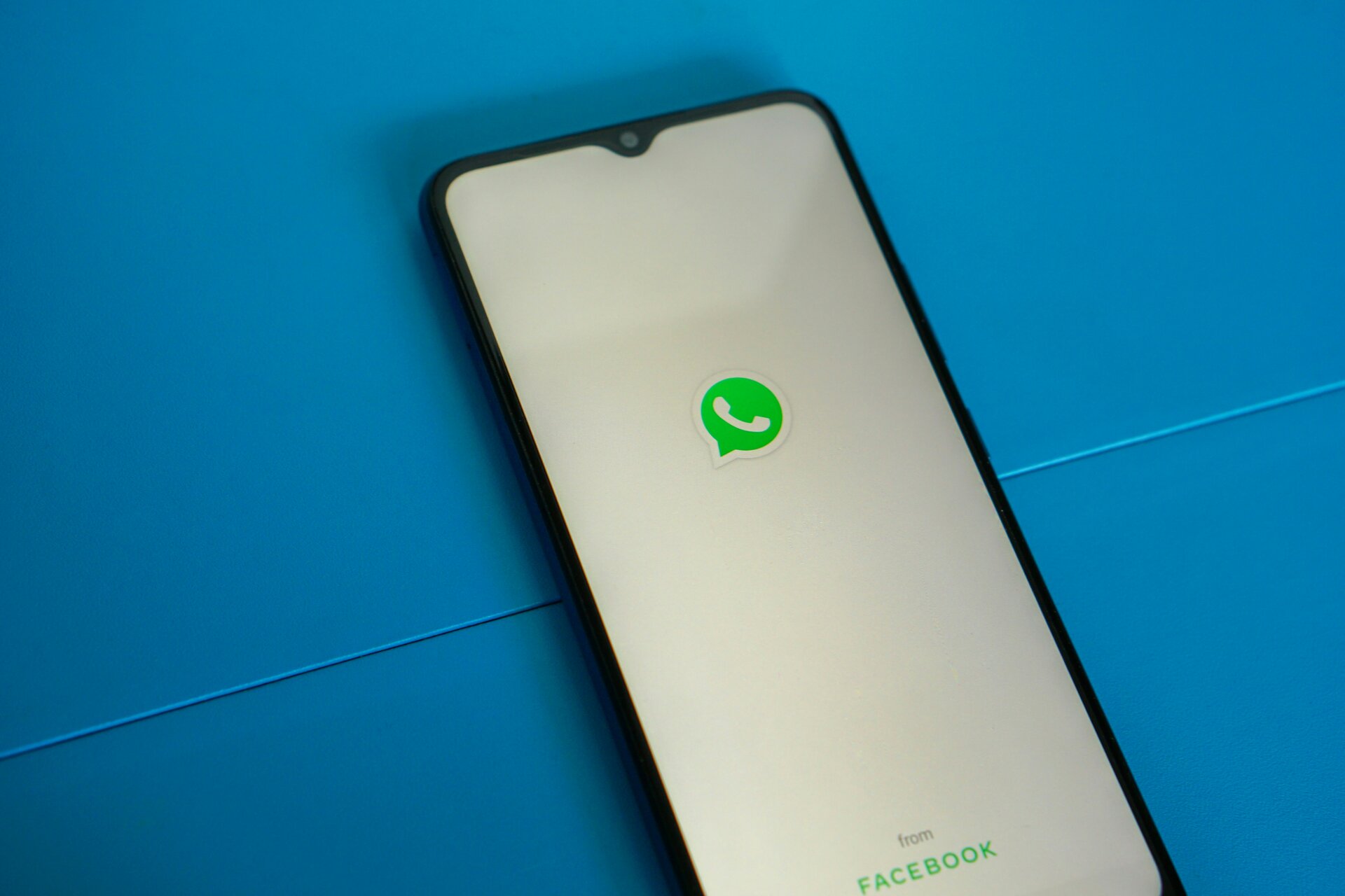 Das Bild zeigt ein Smartphone, auf dem das WhatsApp-Logo zu sehen ist, vor blauem Hintergrund | © Mourizal Zativa/Unsplash