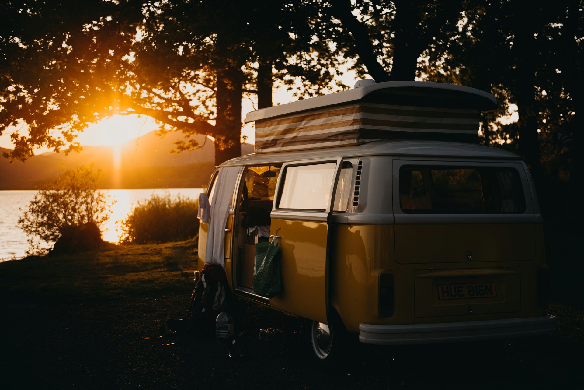 Das Bild zeigt einen alten VW-Bus mit Dachzelt, der in der Dämmerung an einem Seeufer parkt | © Kevin Schmid/Unsplash